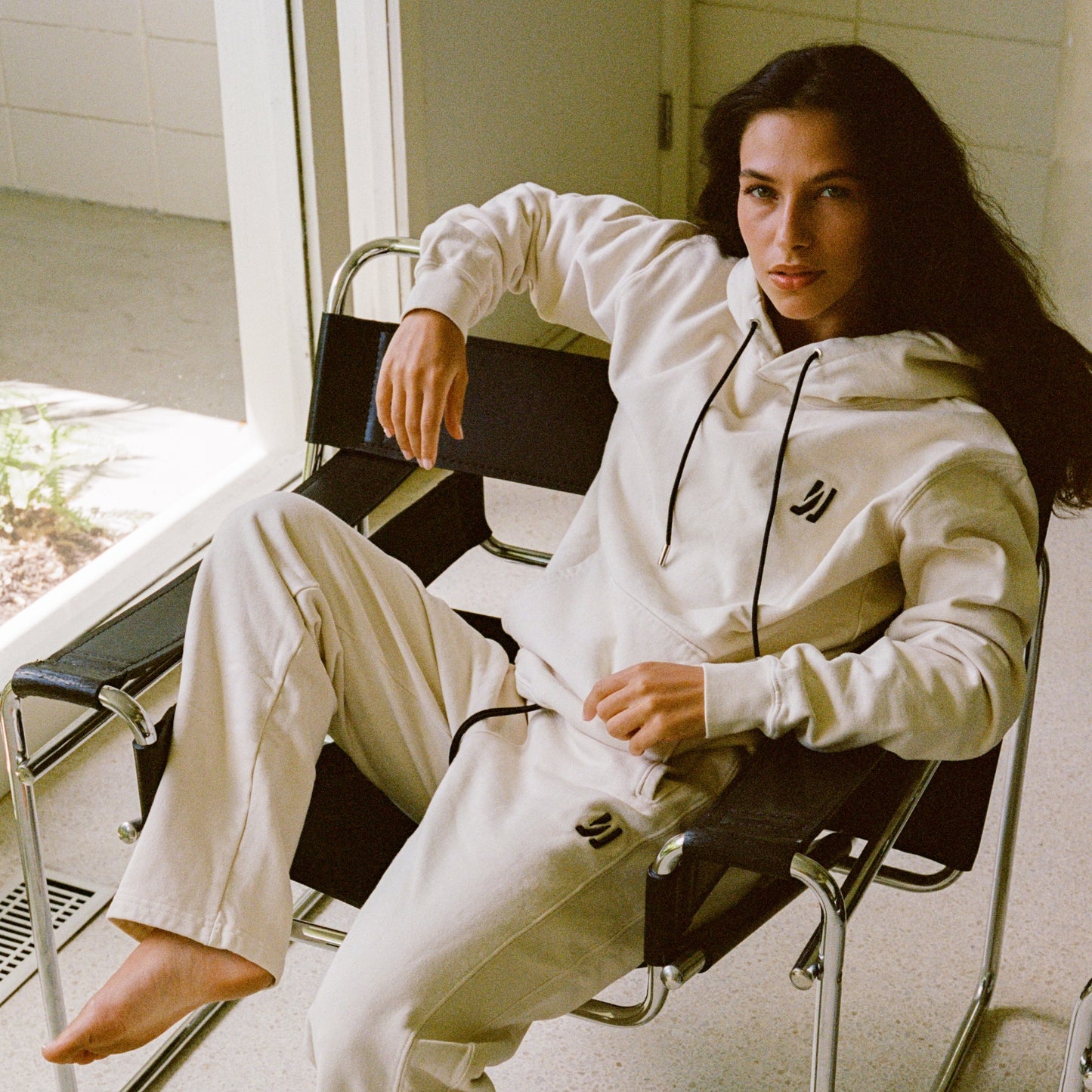 Person wearing a white 'COMUNE' tracksuit sitting on a chair indoors.