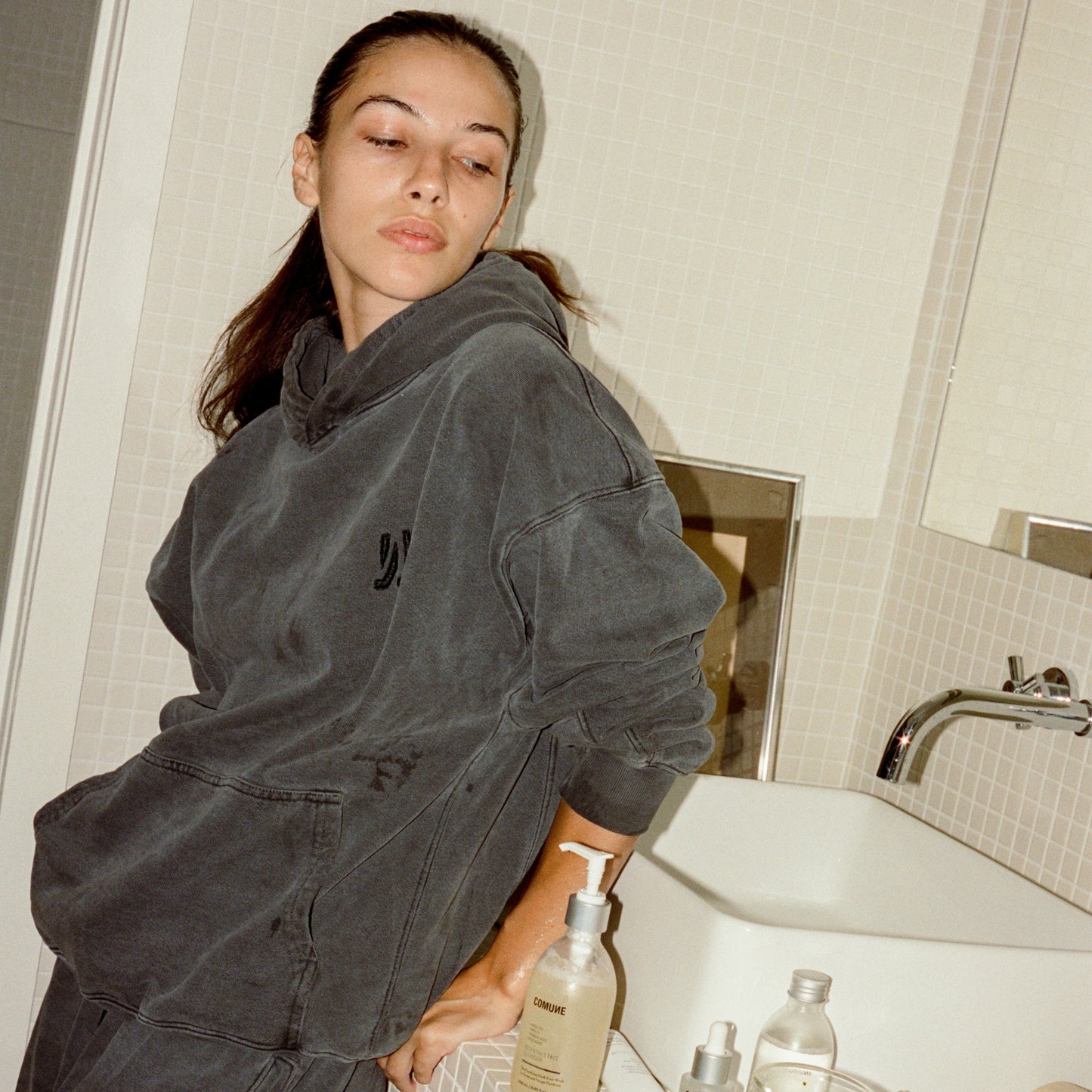 COMUNE model in a bathroom with comune essentials cleanser bottle on the counter