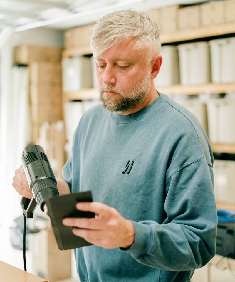 COMUNE artist Jason Gregory from MAKR holding a heat gun curating a leather wallet.