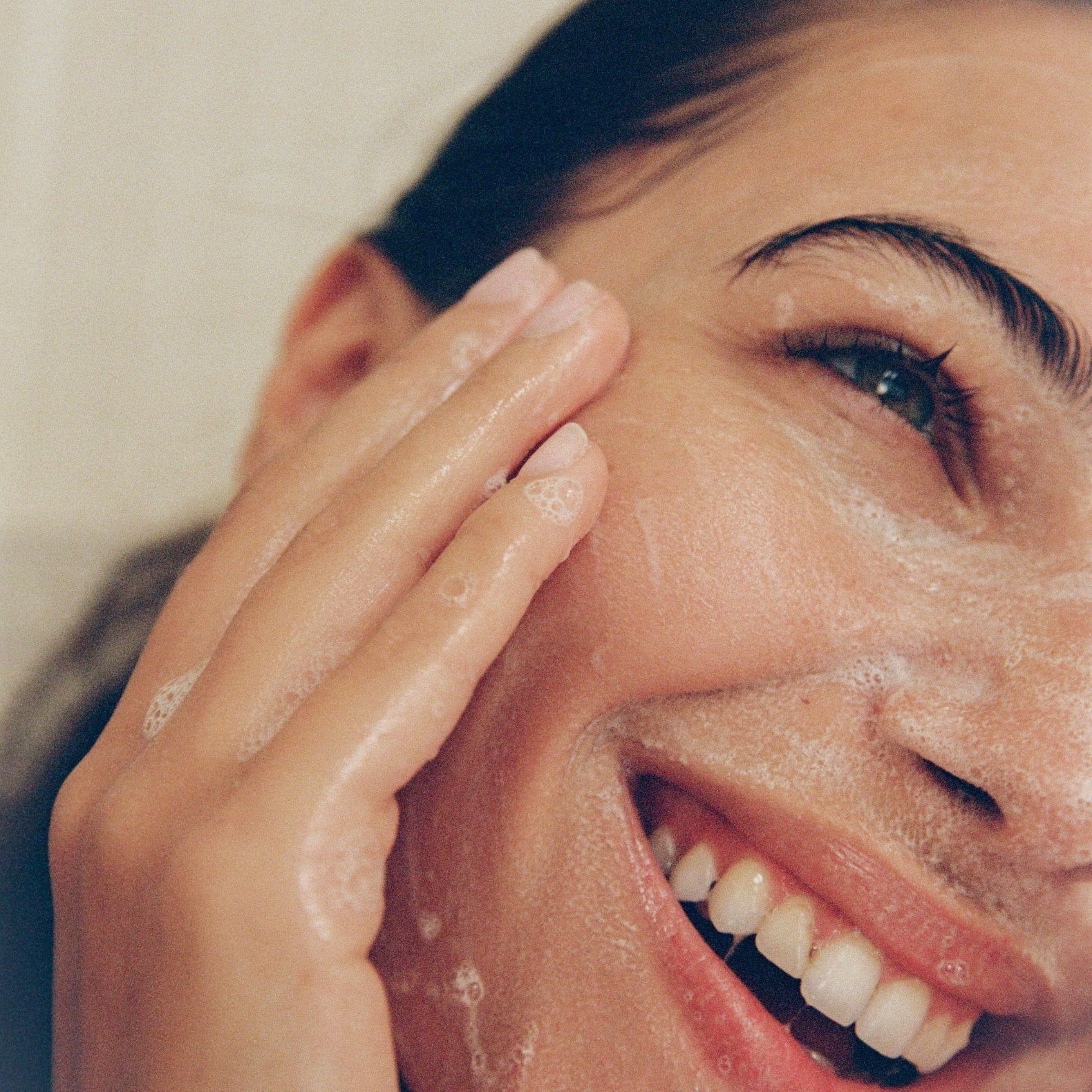 A close up shot of a women cleansing her face with COMUNE Essentials Face Cleanser.