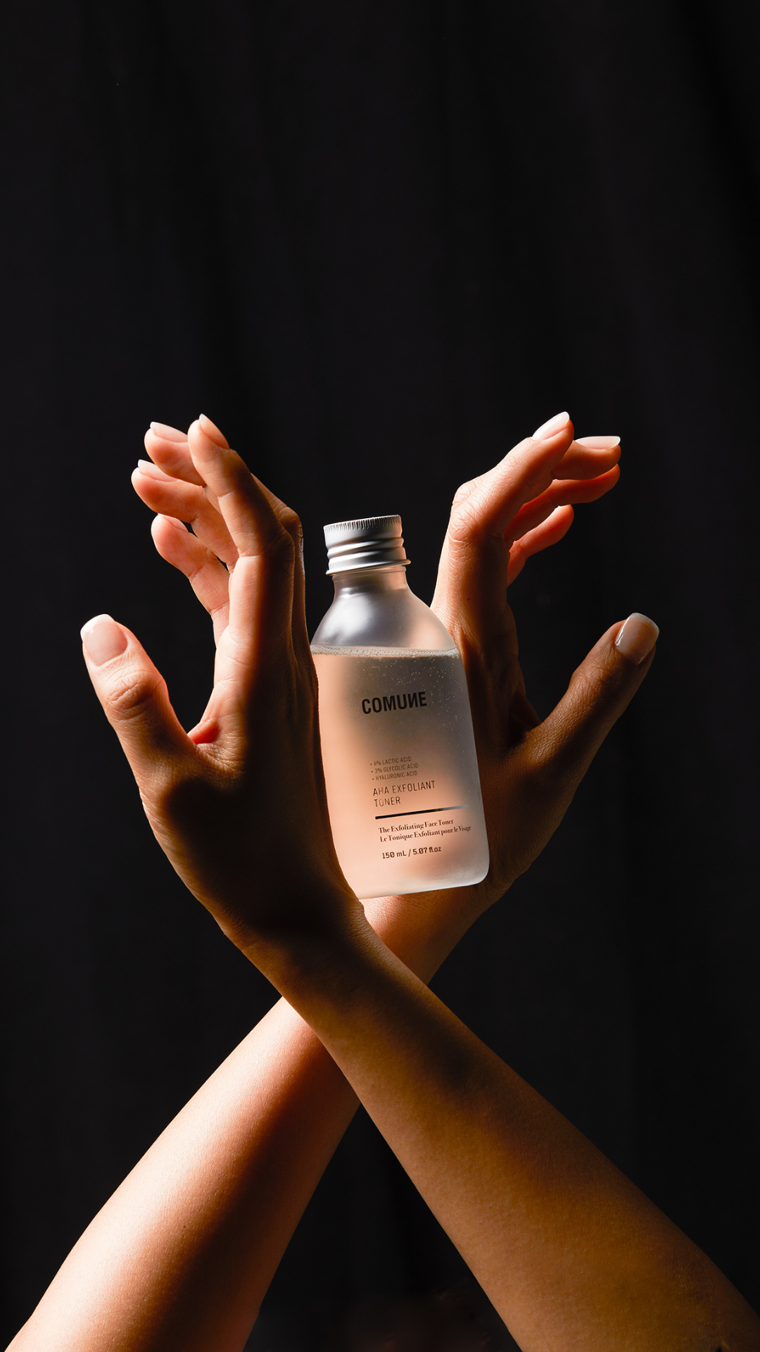 Comune AHA Exfoliant Toner held by a women's hand expressing angel wings