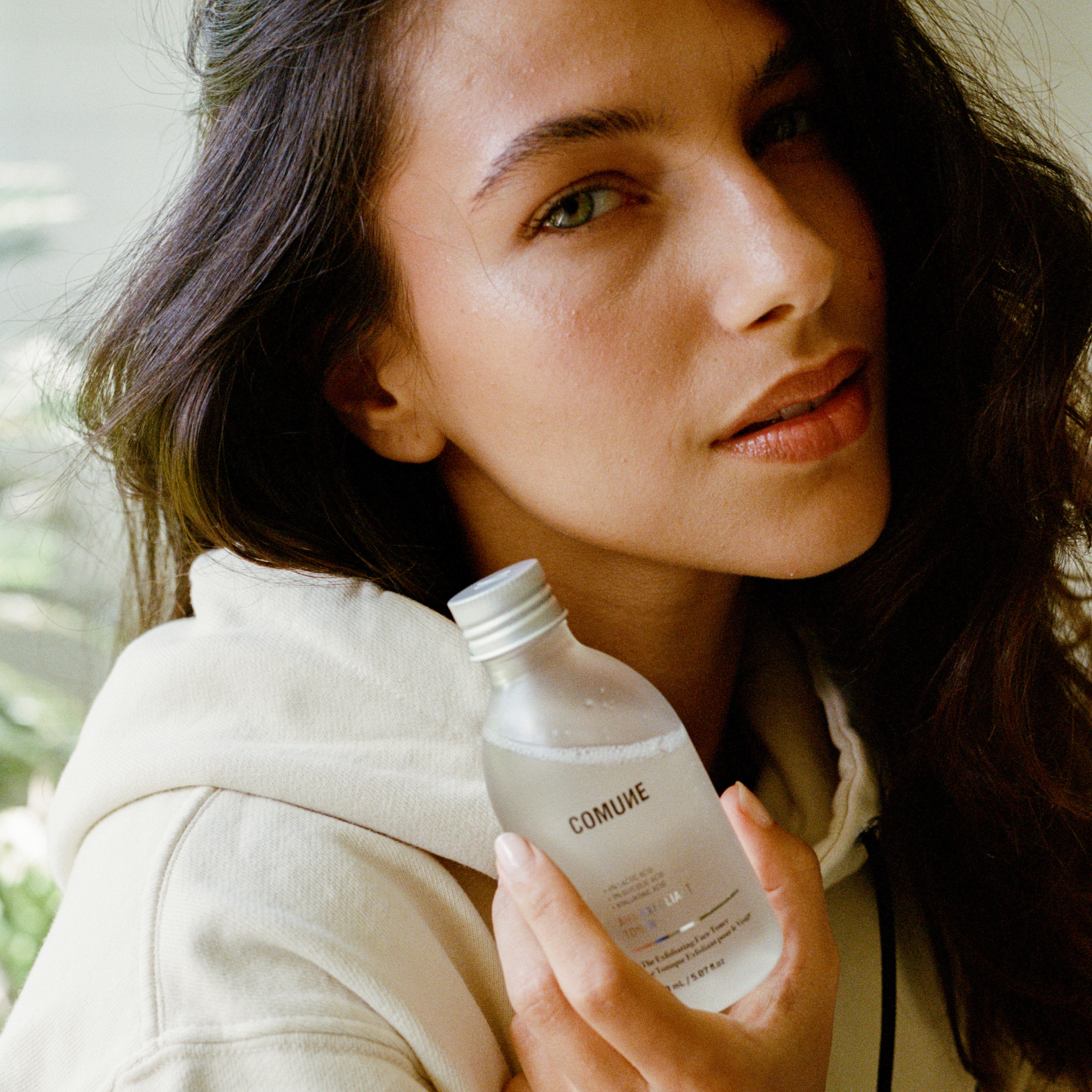 Woman holding a bottle labeled 'COMUNE' with a blurred natural background