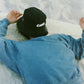 Person wearing a comune black bucket hat with 'Comune' logo and Comune Duke blue sweatshirt lying at the beach..
