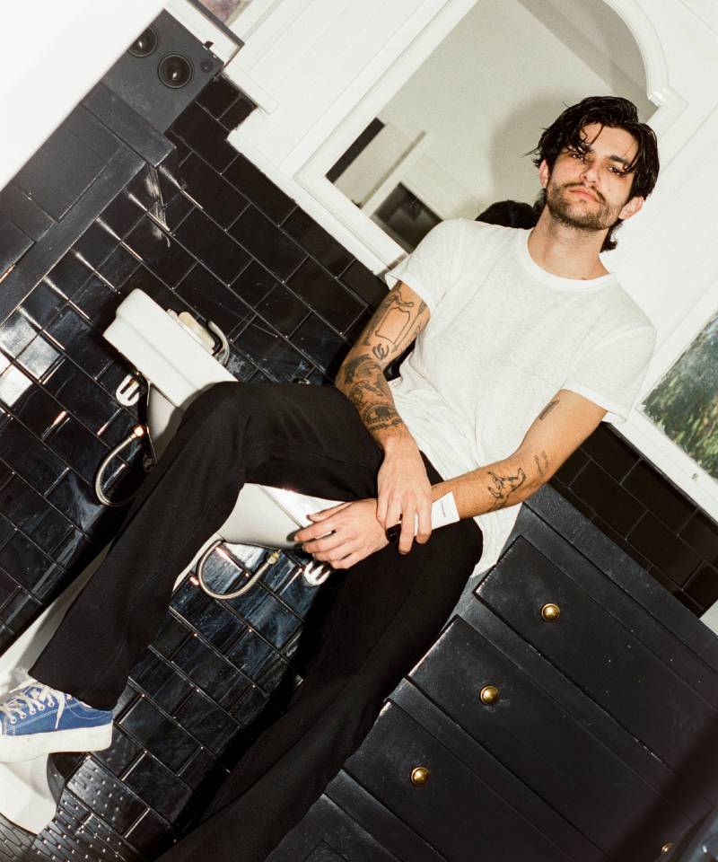 COMUNE artist Brandon Shoop sitting on a black tiled floor with a white wall in the background