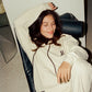 Person wearing a 'COMUNE' white hoodie sitting on a black chair indoors.