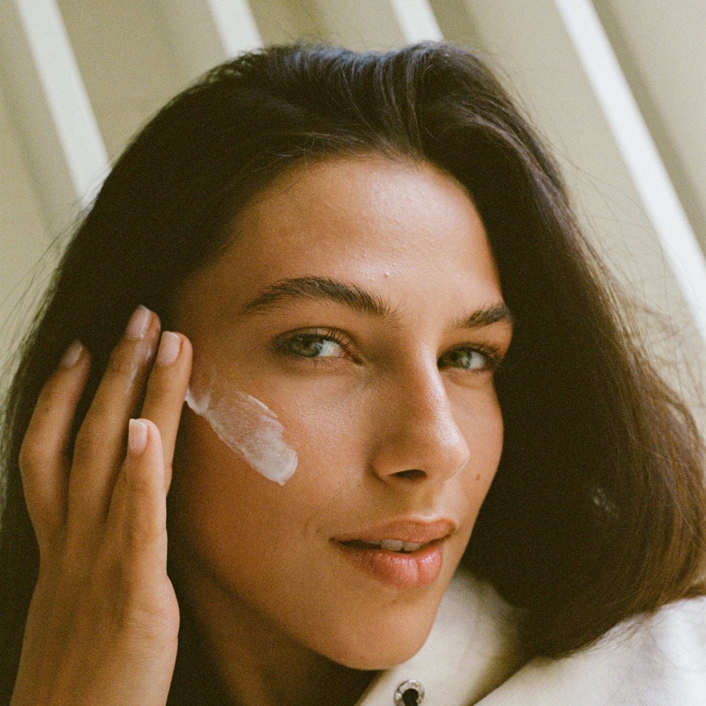 Woman applying cream to her face with a neutral background