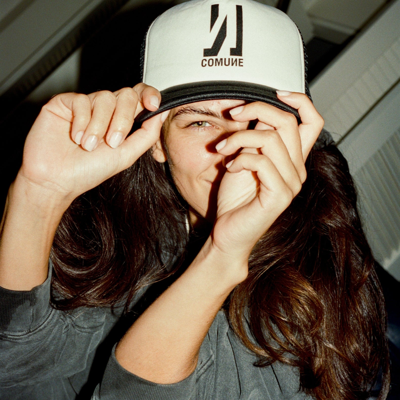 Person wearing a cap with 'COMUNE' logo, holding it over their face.