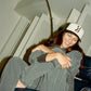 Person wearing a cap with a 'COMUNE' logo, sitting indoors.