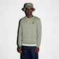 A model wearing a sage color COMUNE Luka Crew sweatshirt with a small black embroidered logo on the left chest, paired with a matching army green bucket hat and dark blue jeans, standing against a plain white background.