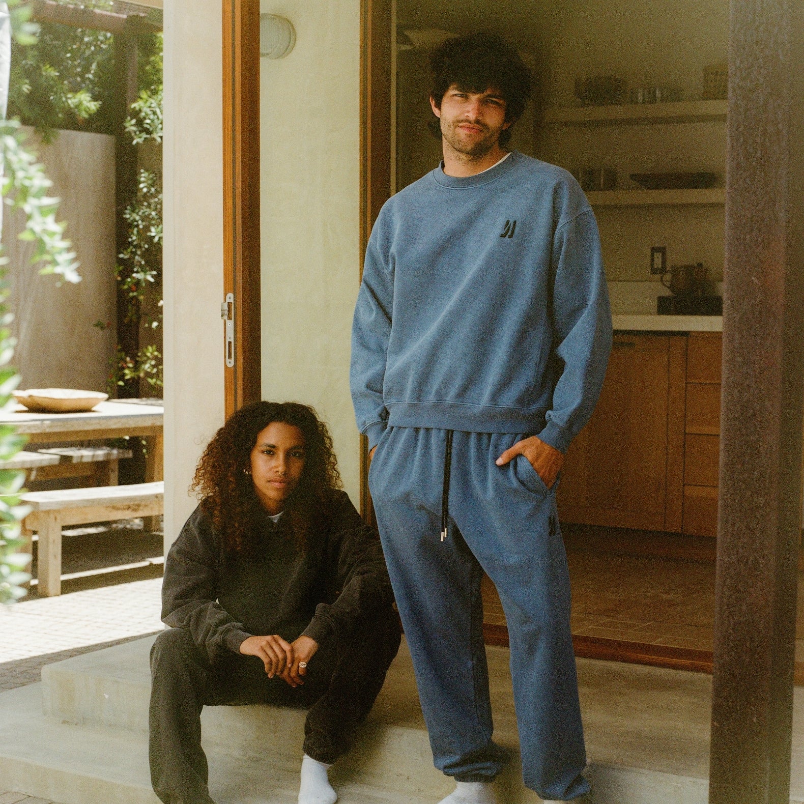 Two people in matching blue tracksuits standing in a modern kitchen, women wearing Duke hoodie and Enzo joggers in faded black color, and man wearing Duke crew and Enzo joggers in marine color. COMUNE Enzo Jogger | Marine
