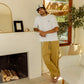 Man standing in a living room with a fireplace and a plant, wearing the Nori Tee in white color and Enzo joggers heavyweight cotton in acorn color. COMUNE Enzo Jogger | Acorn