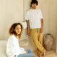 Two people in a room with a neutral color scheme, one sitting and one standing. Man wearing Nori Tee in white color and Enzo joggers in acorn color, women wearing white color Luka Crew. COMUNE Enzo Jogger | Acorn