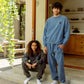 Two people in the patio infront of the open kitchen, women sitting on a step wearing faded black Duke Hoodie and Enzo Joggers, and the men stending next to her wearing Duke Crew and Enzo Joggers in Marine color. COMUNE Duke Crew | Marine