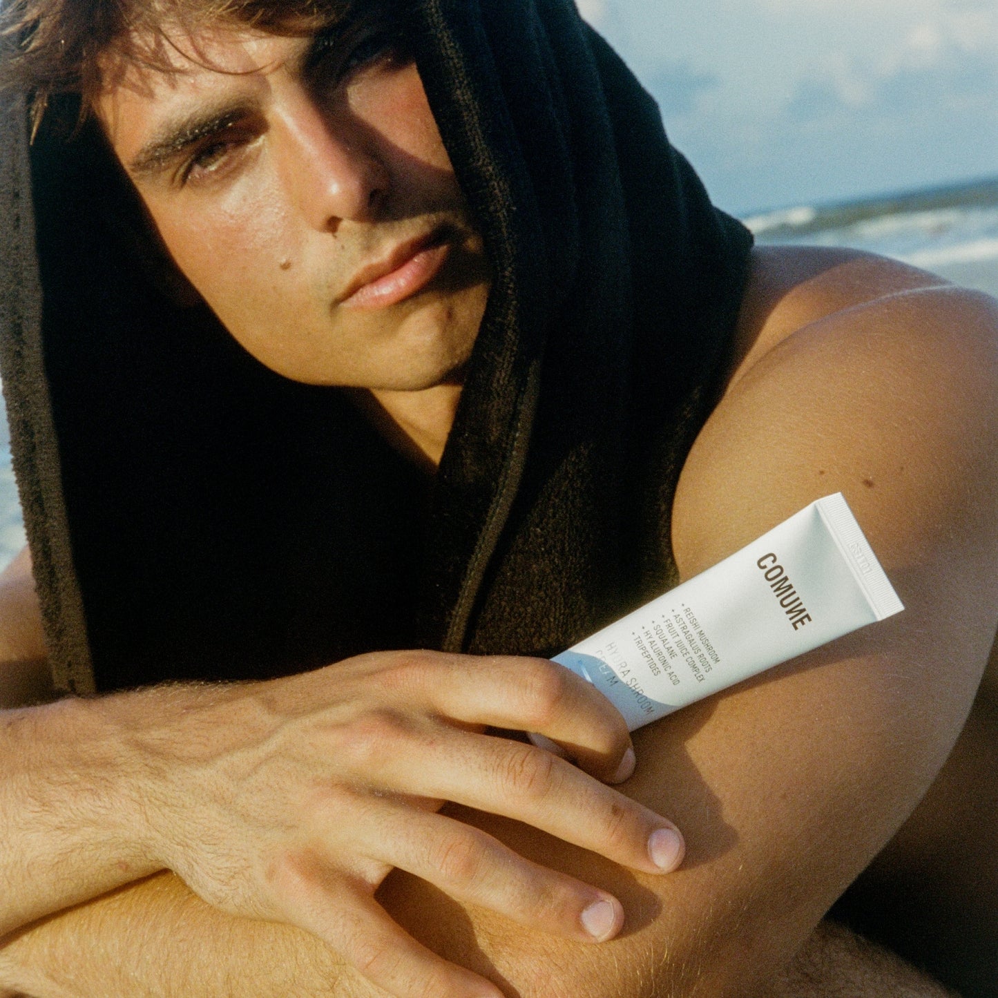 Man showcasing COMUNE Hydra Shroom Cream  on a beach
