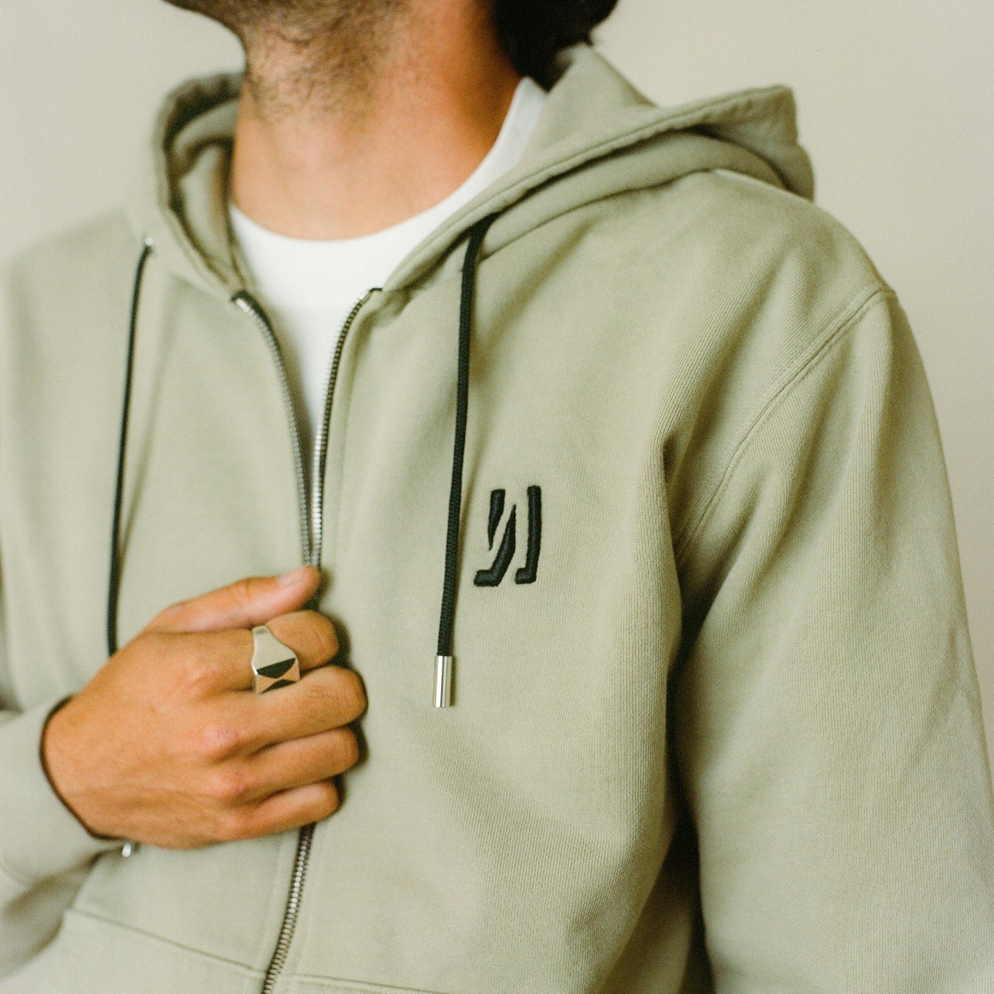 A close up of the Comune logo embroidered in front of the Comune Luka Zip-up heavyweight cotton hoodie in a sage color. COMUNE Luka Zip-up | Sage