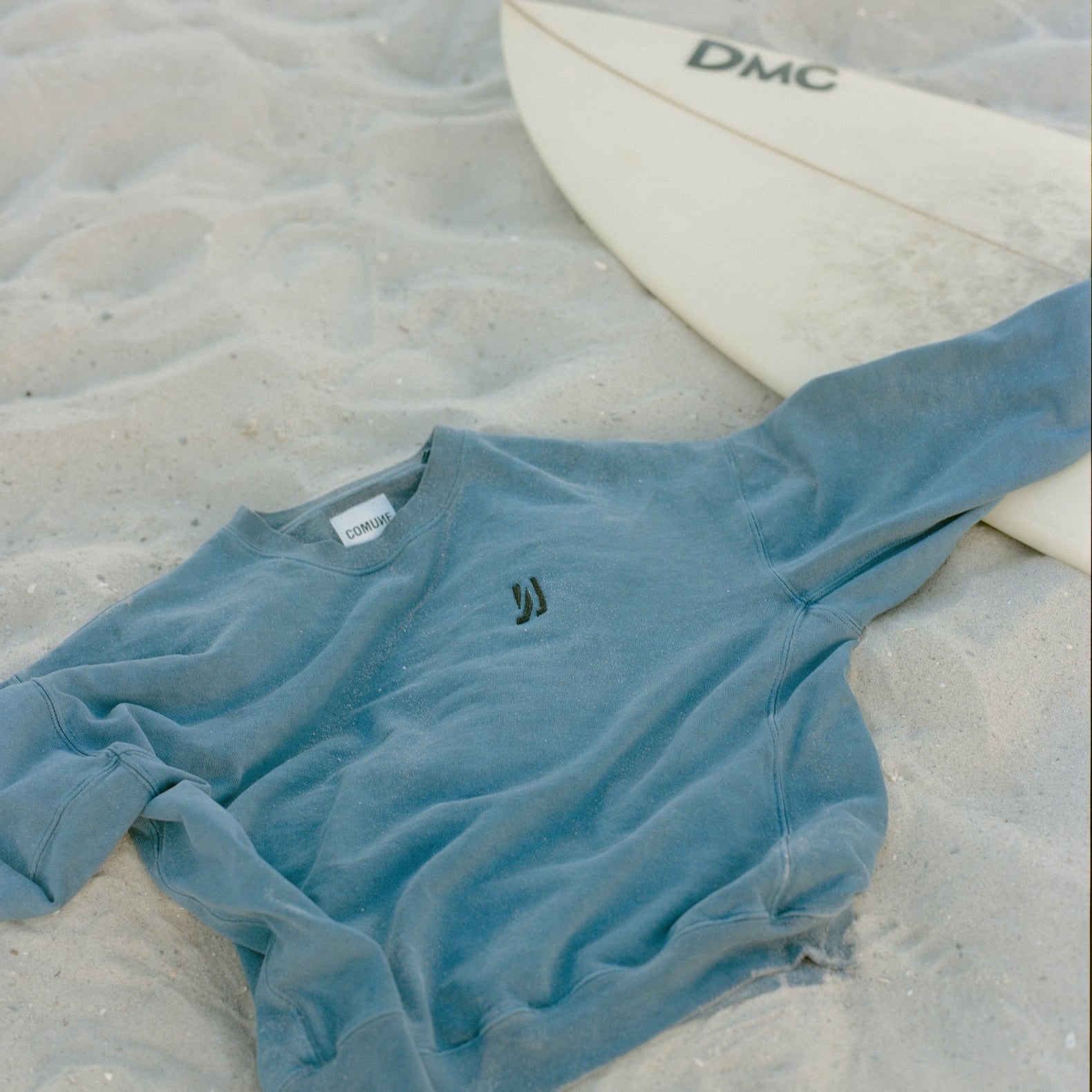 Comune Duke Crew heavyweight cotton sweatshirt, laying down on a sand next to a surfboard at the beach. COMUNE Duke Crew | Marine