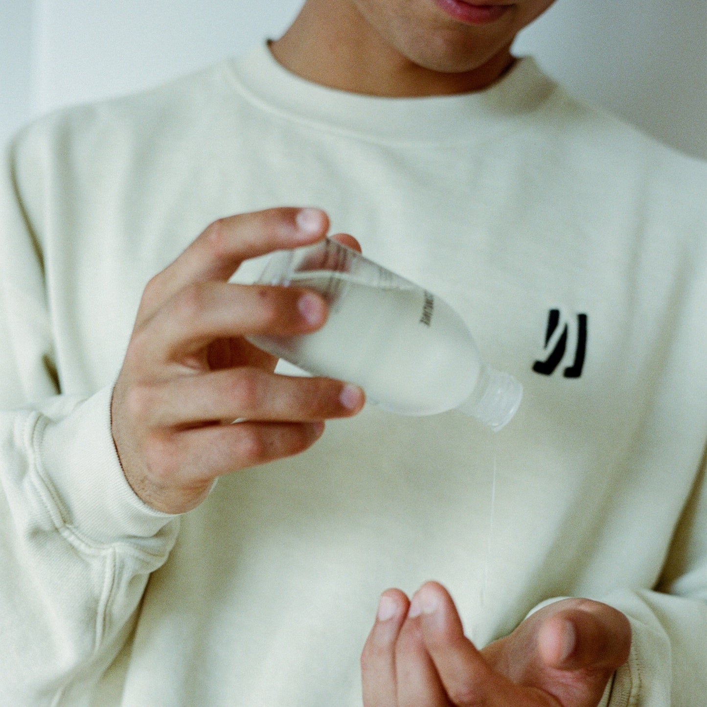 Person wearing a Comune Duke crew sweatshirt with a logo, holding a Comune AhA Exfoliant Toner getting to apply. Clean, natural, vegan & cruelty-free. 
