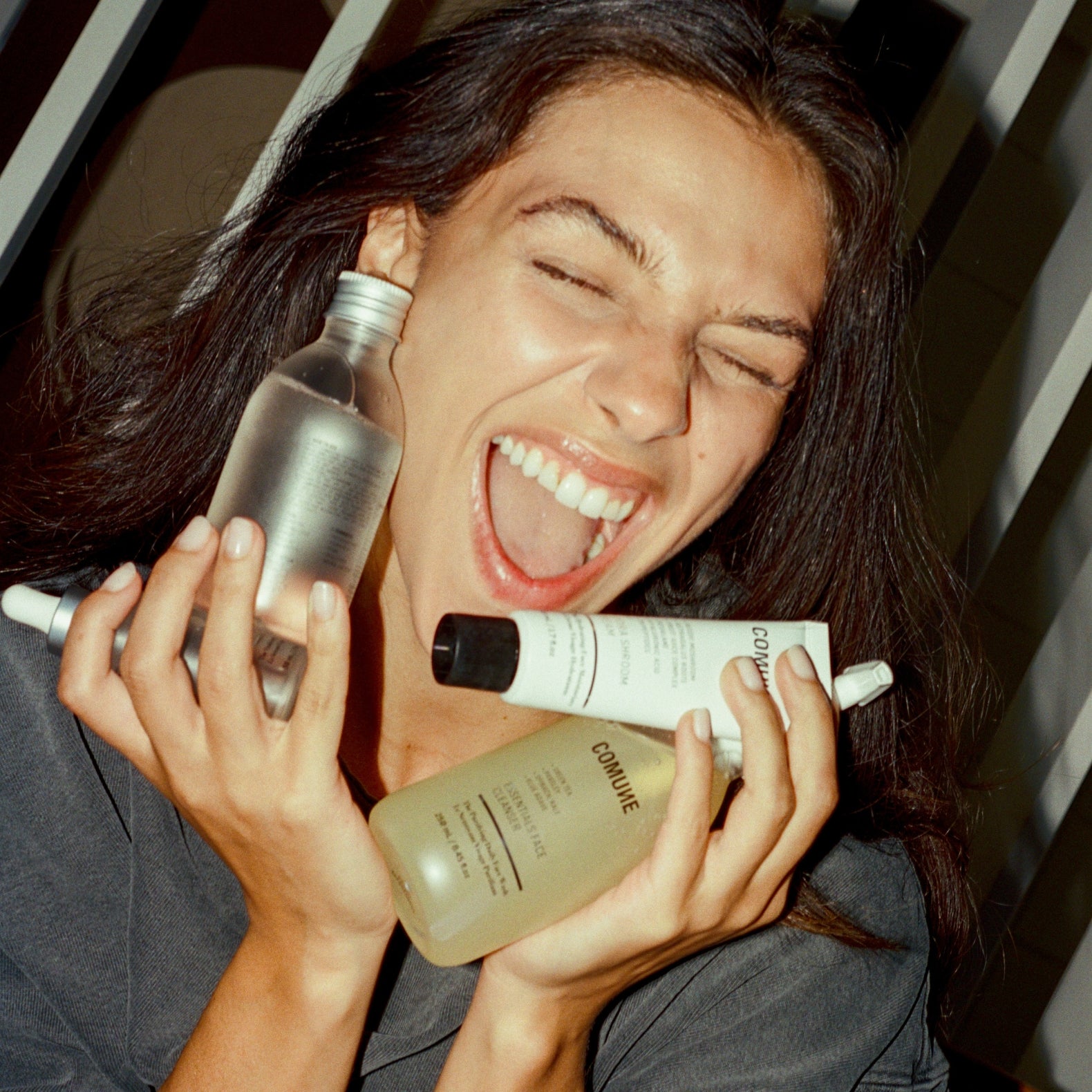 Woman holding and smiling with 'COMUNE' skincare bottles