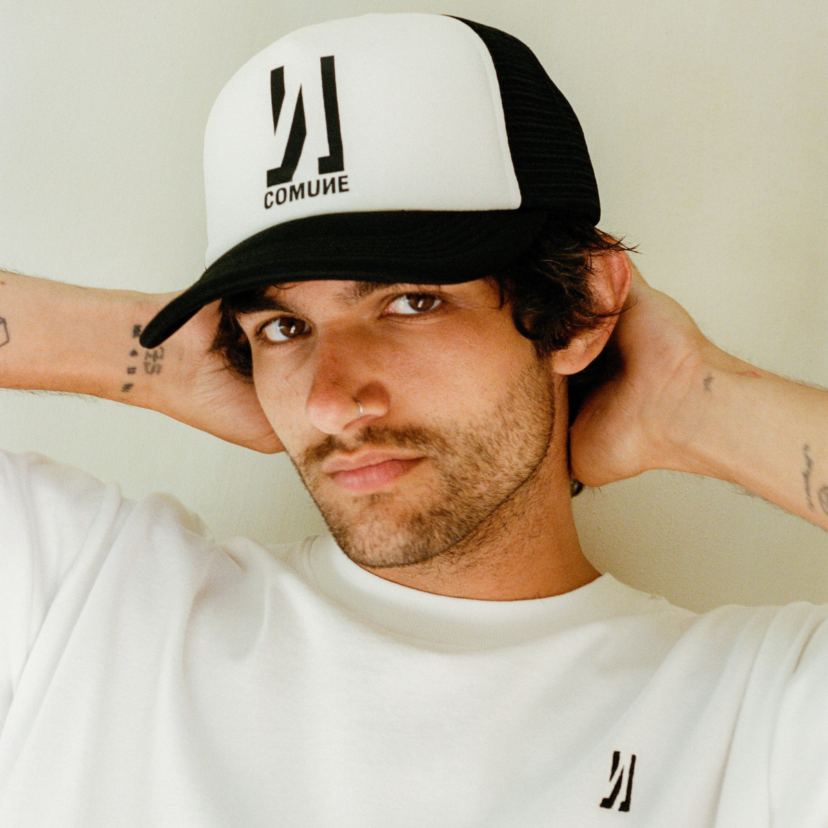 Man wearing a white and black cap with 'COMUME' branding, posing against a plain background.