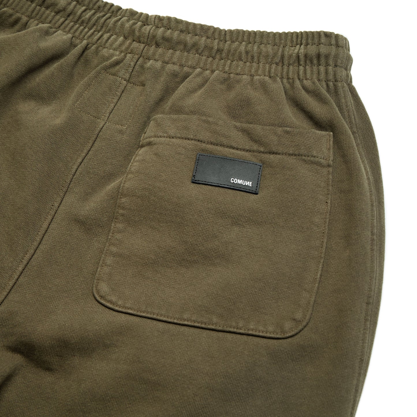 Comune Duke Sweatpants in heavyweight cotton with side gusset in army green color on white background, leather patch close up. COMUNE DUKE SWEATPANTS | Army Green