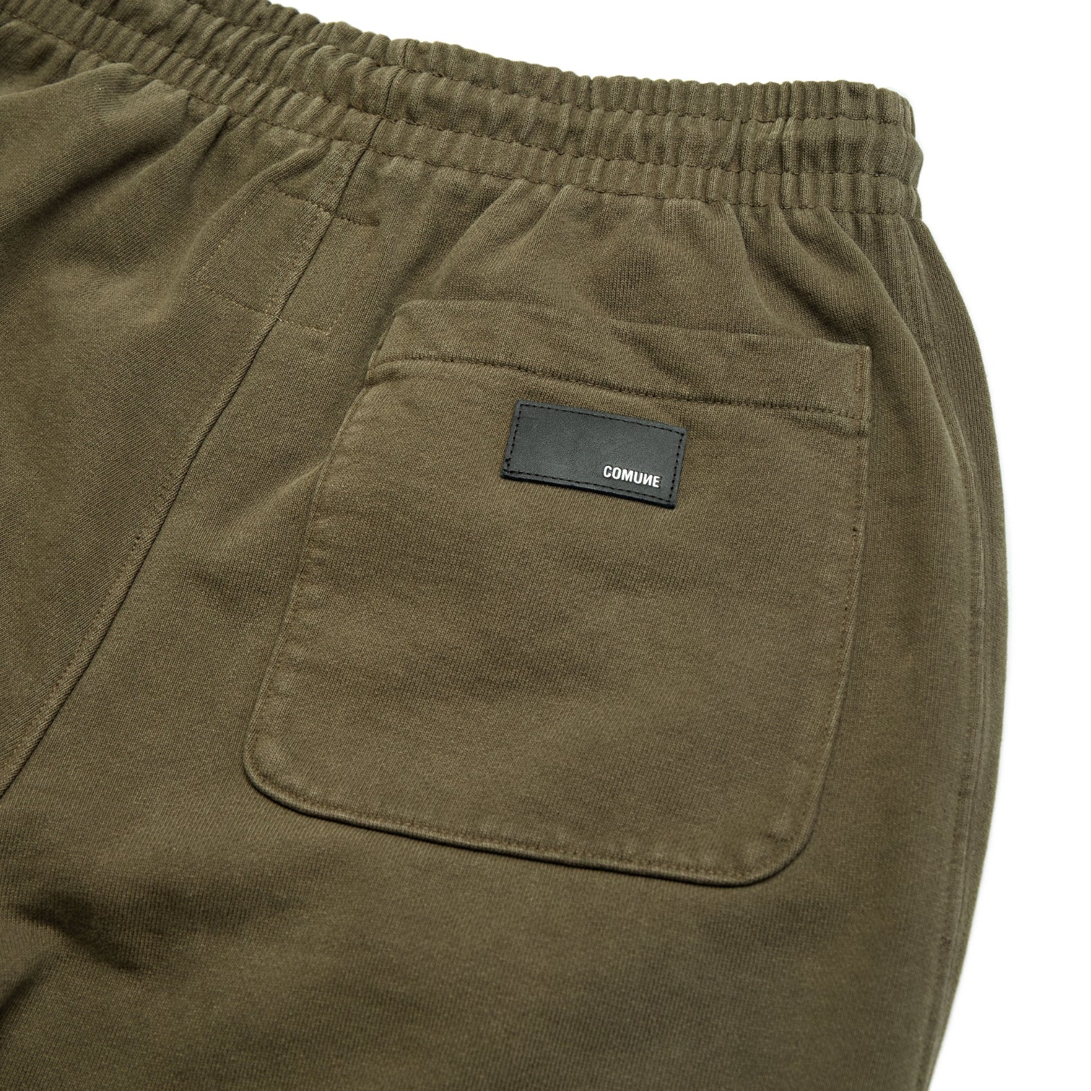 Comune Duke Sweatpants in heavyweight cotton with side gusset in army green color on white background, leather patch close up. COMUNE DUKE SWEATPANTS | Army Green