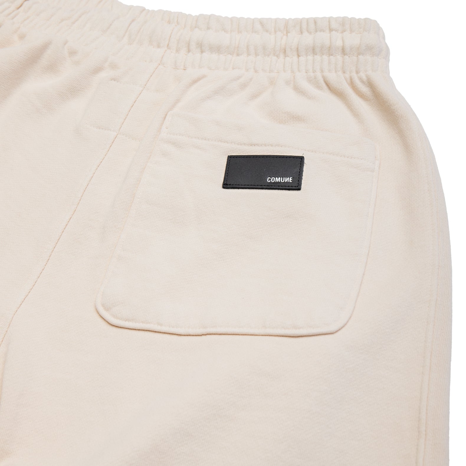 Comune Duke Sweatpants in heavyweight cotton with side gusset in bone color on white background, leather patch close up. COMUNE DUKE SWEATPANTS | Bone