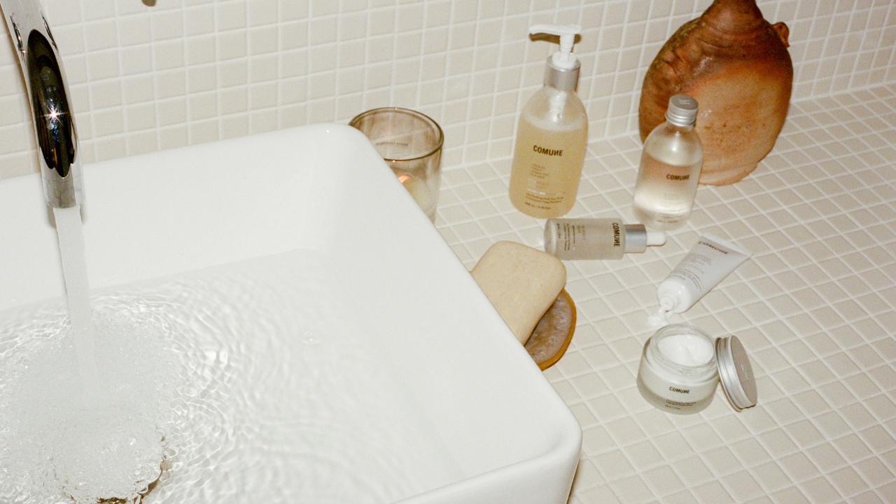 Bathroom scene with a bathtub, toiletries, 'COMUNE' Essentials Skincare products, and a tiled wall.