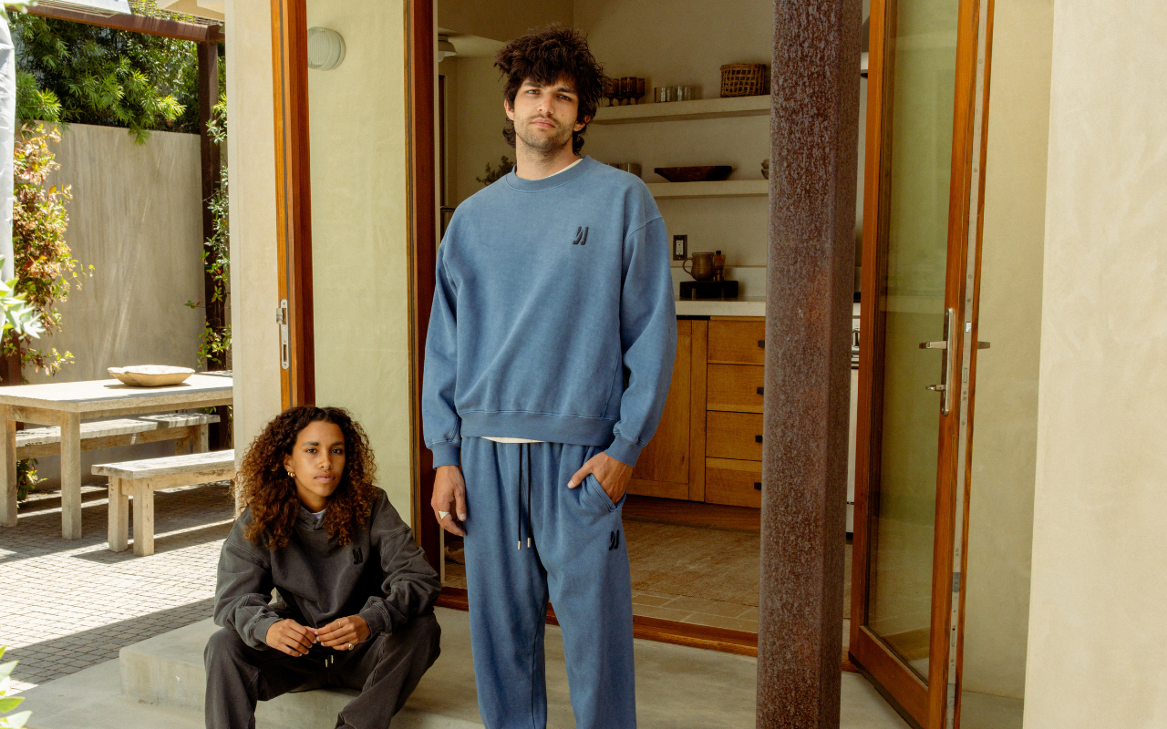 Two people wearing matching blue tracksuits standing in a modern kitchen wearing COMUNE clothing.