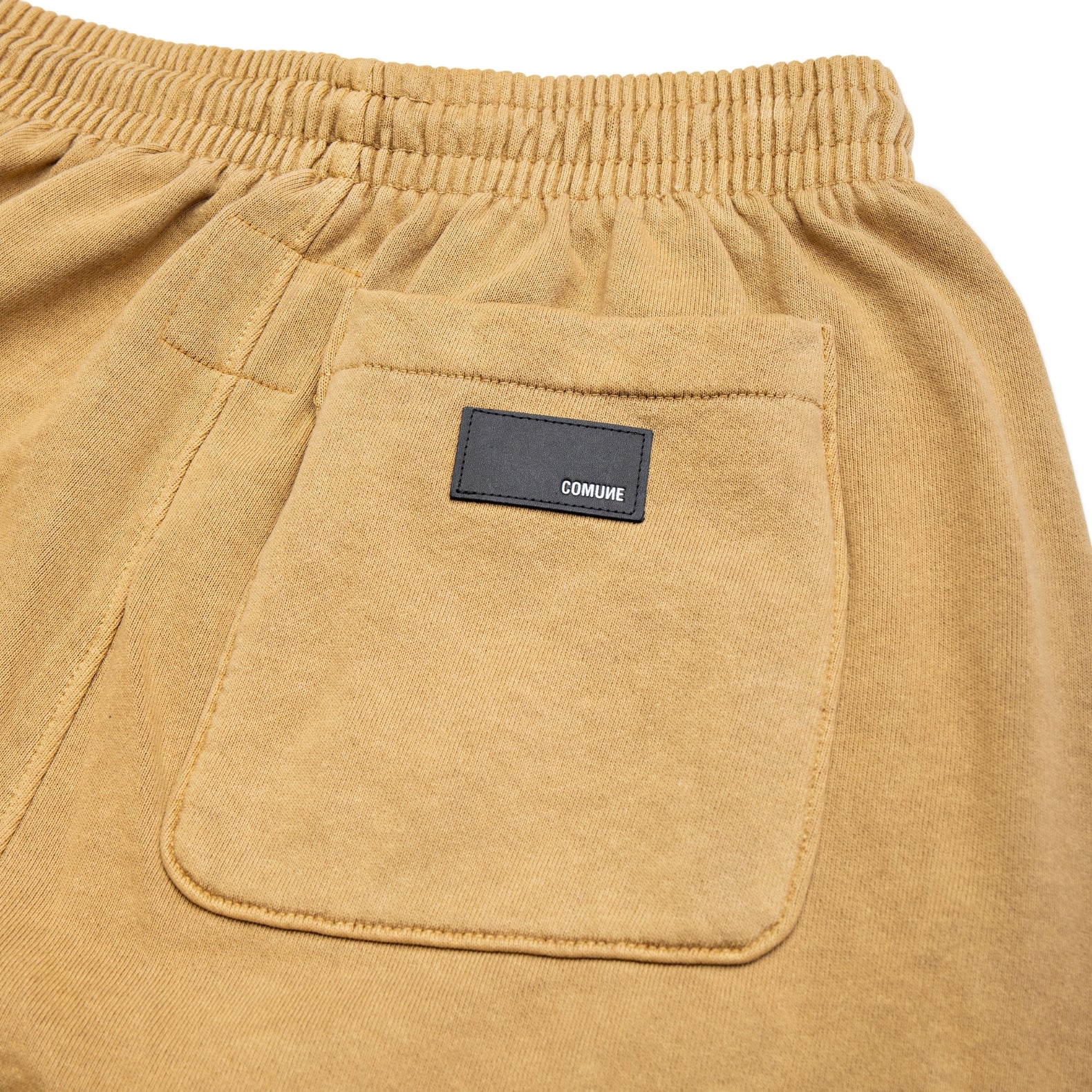 Comune Enzo Joggers heavyweight cotton in acorn color on white background, leather patch. COMUNE ENZO JOGGER | Acorn