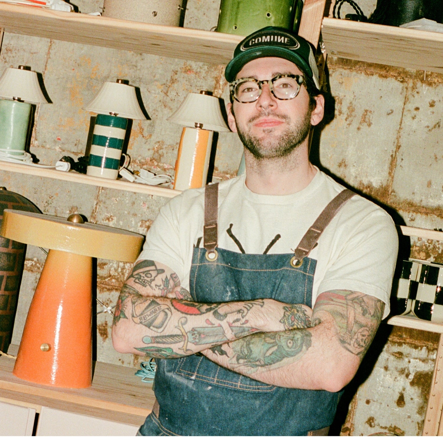 COMUNE artist Ethan Streicher standing in a workshop with shelves of lamps.