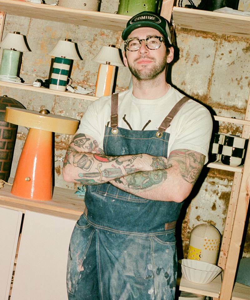 COMUNE artist Ethan Streicher wearing a cap and apron with tattoos standing in a workshop.