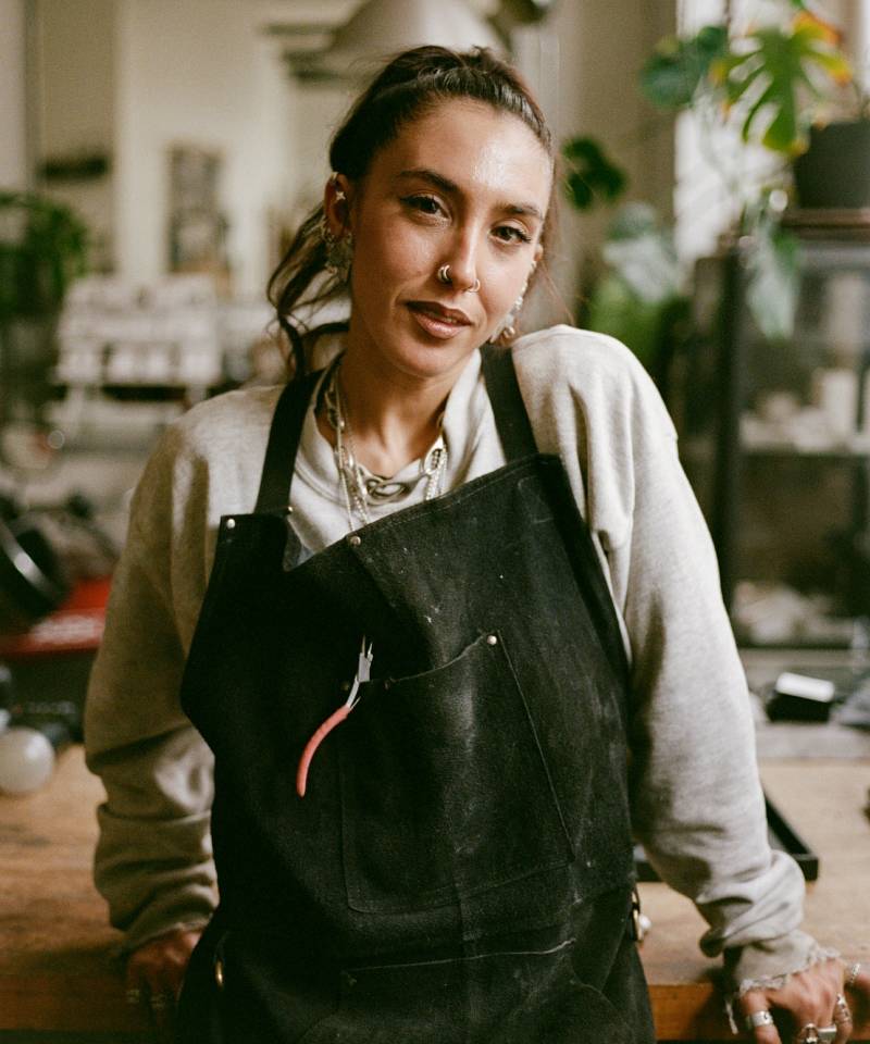 Person wearing a black apron in an indoor setting with plants and furniture.