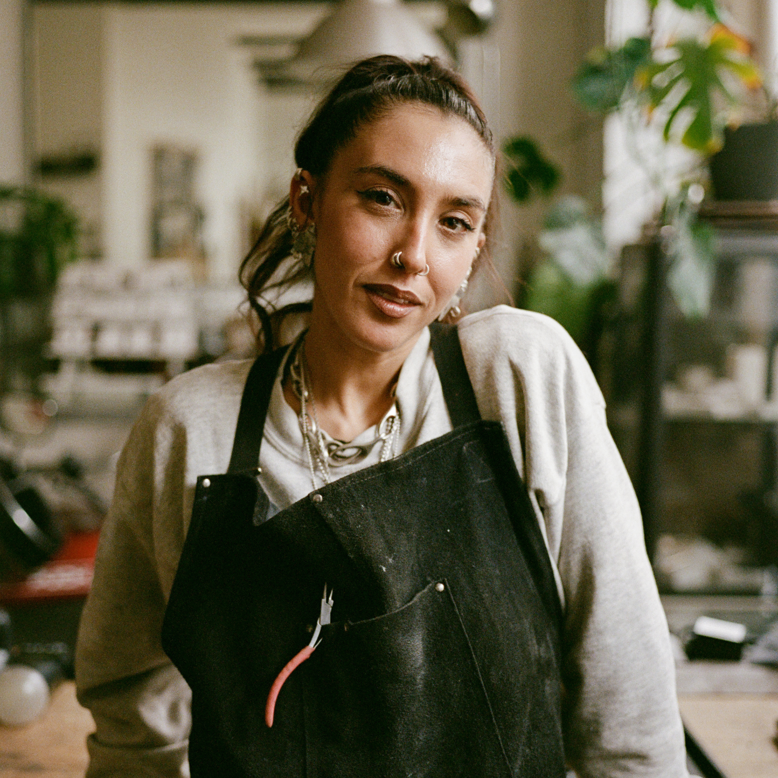 COMUNE Artist Lizz Jardim posing at her work place wearing an apron where she works creating jelwery.