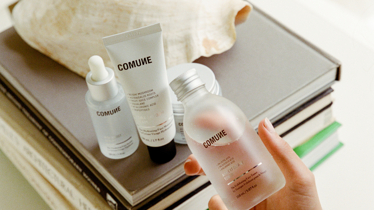 COMUNE skincare products on books with a hand holding a bottle