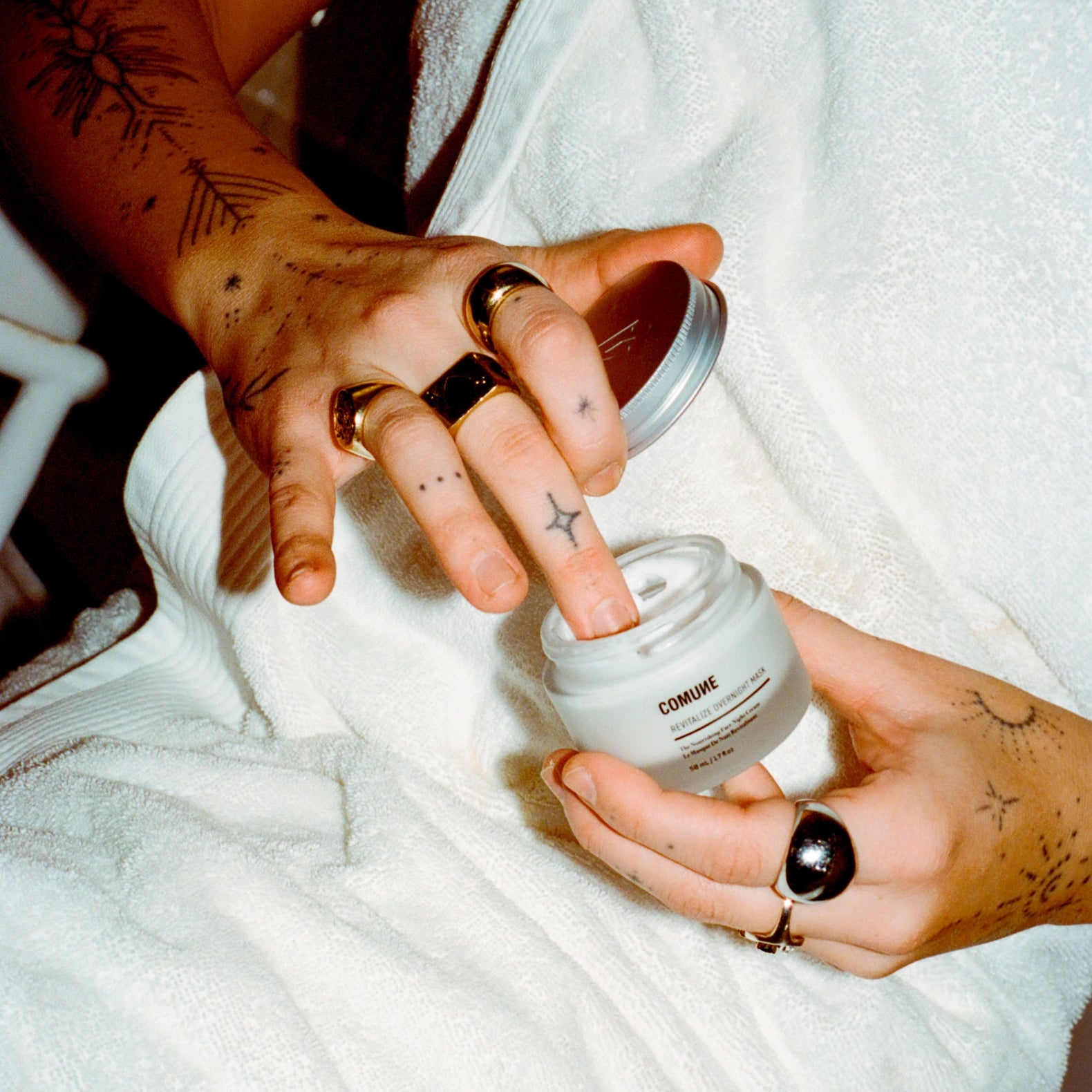 Person holding a white container labeled 'COMUNE' with a tattooed hand.