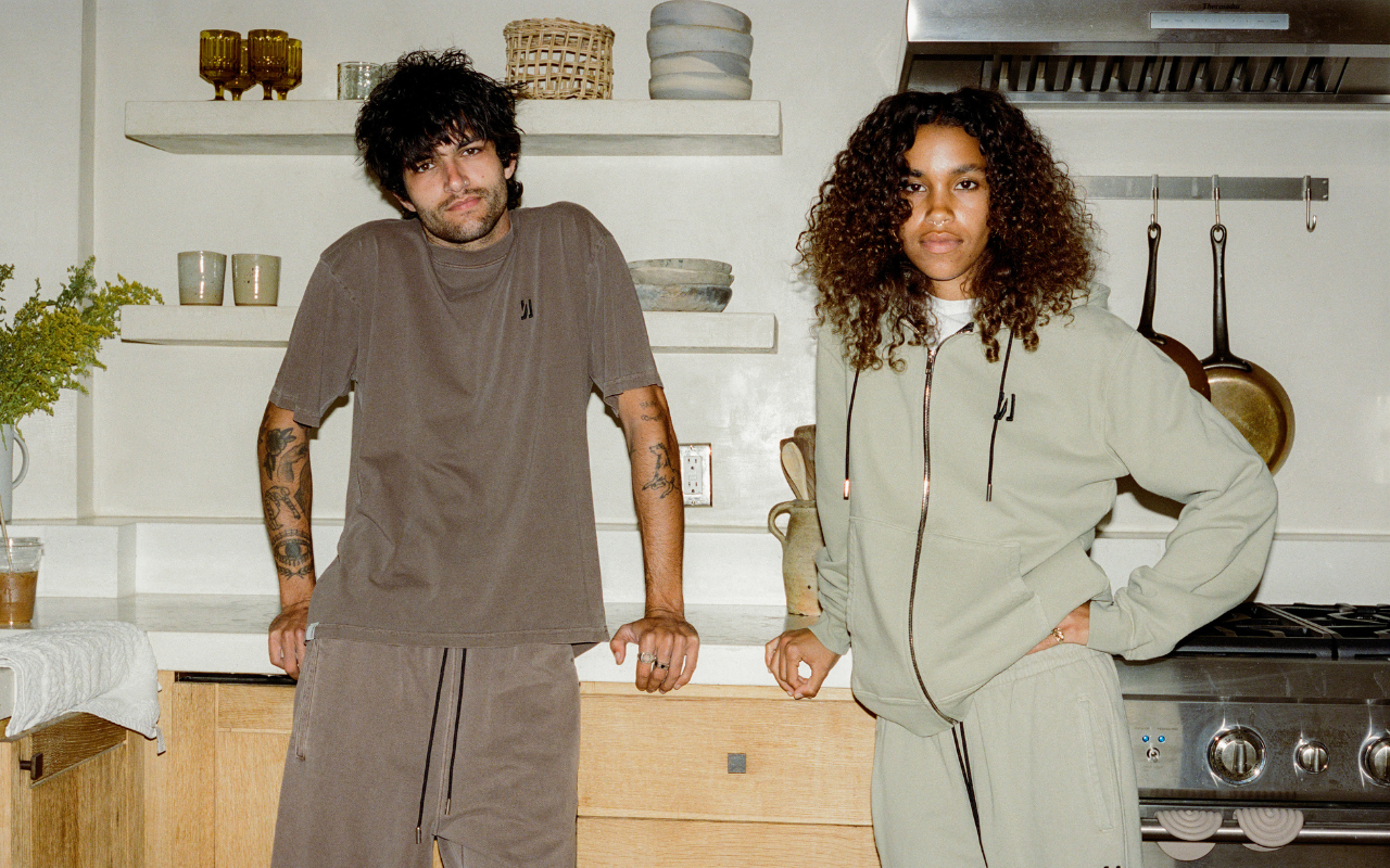 Two people standing in a kitchen, wearing COMUNE clothing.