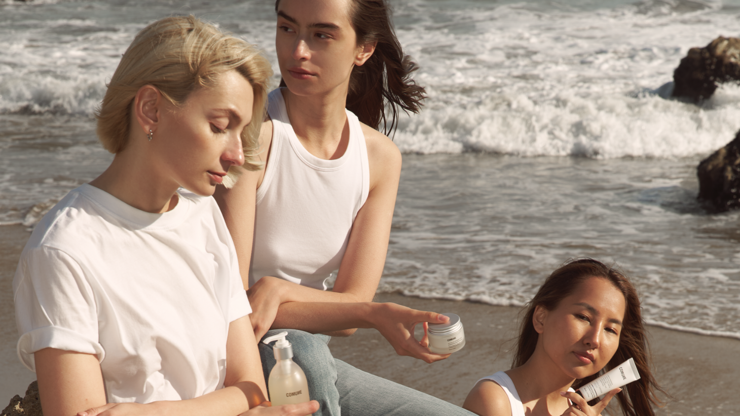 Comune Essentials Skincare showcased by three women sitting at the beach