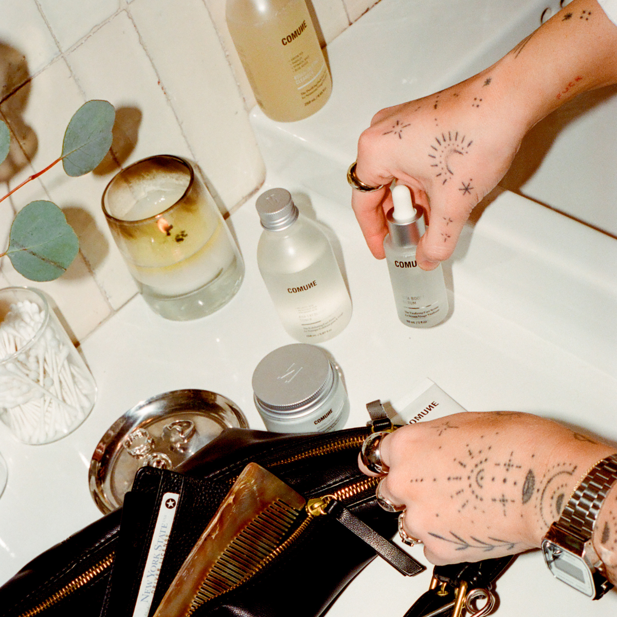 COMUNE model holding a comune skincare product with various bottles and a candle on a white surface