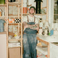 COMUNE artist Ethan Streicher in a pottery studio holding a ceramic bowl with shelves of pottery in the background