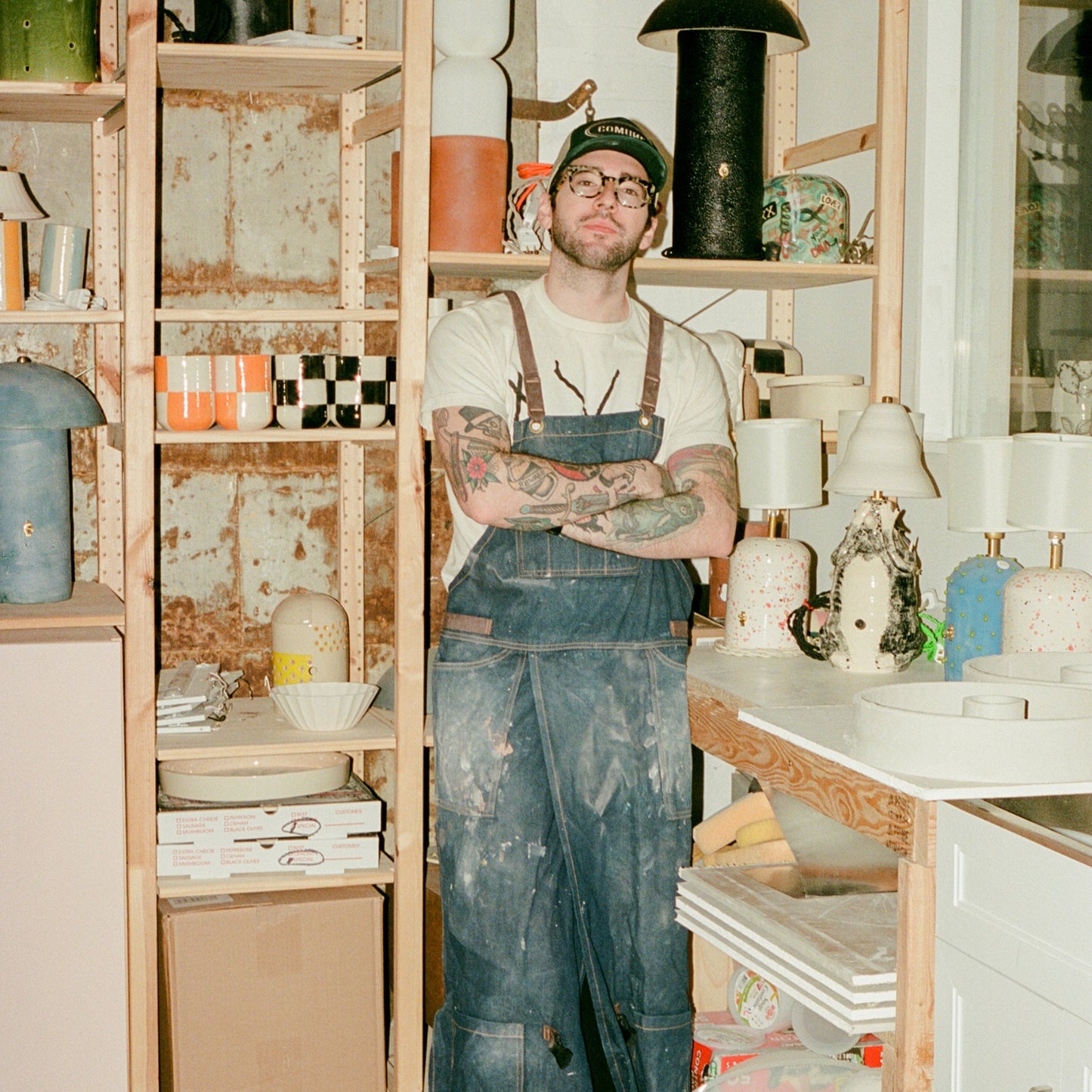COMUNE artist Ethan Streicher in a pottery studio holding a ceramic bowl with shelves of pottery in the background