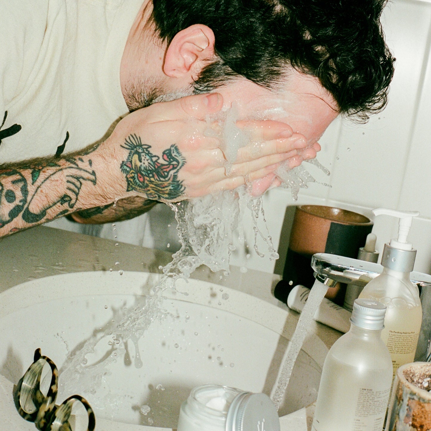 COMUNE artist Ethan washing his face with 'COMUNE' Essentials Face Cleanser in a bathroom setting
