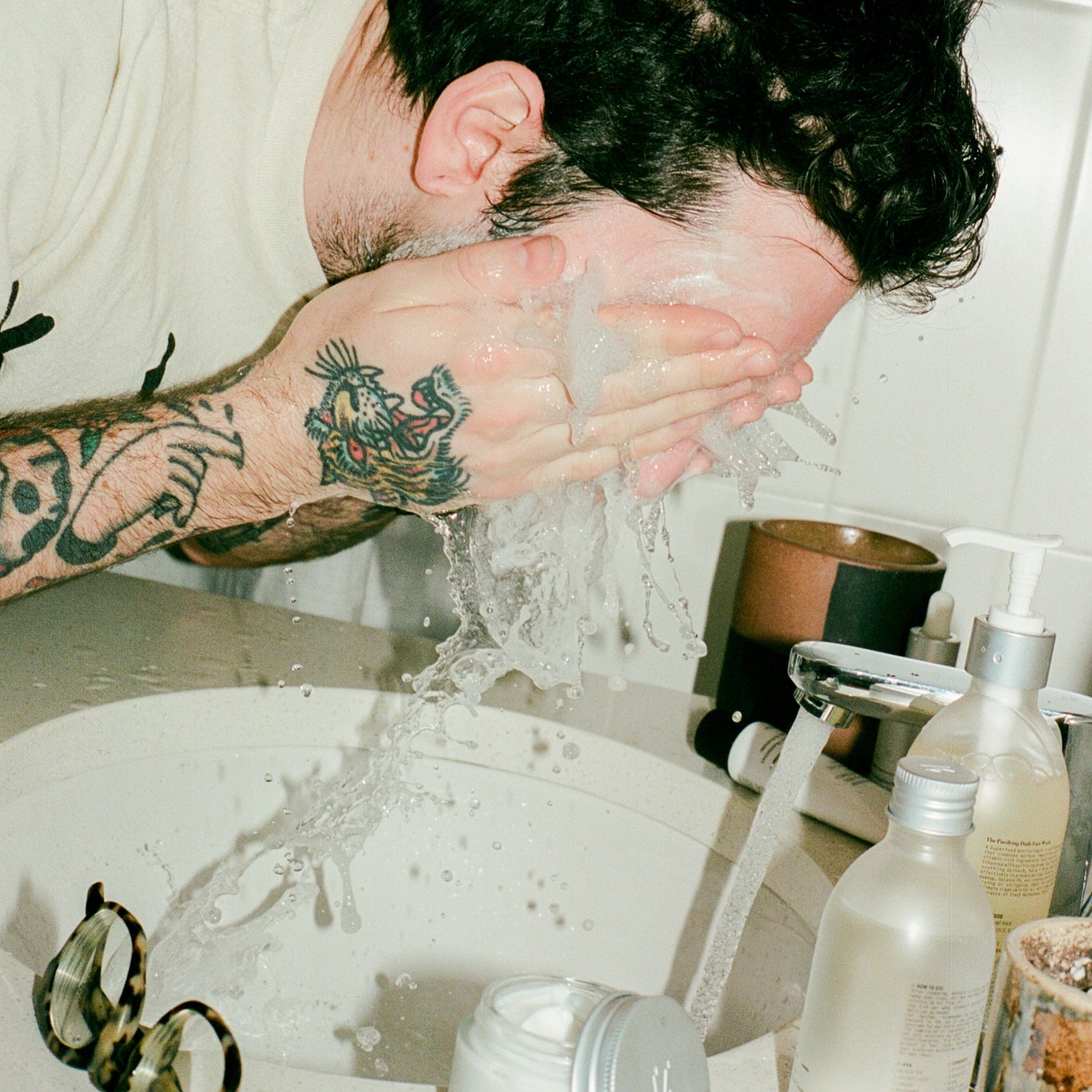 COMUNE artist Ethan washing his face with 'COMUNE' Essentials Face Cleanser in a bathroom setting