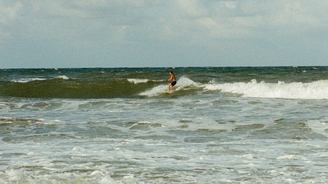 Person surfing on a wave in the ocean with a cloudy sky.