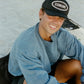 Surfer wearing COMUNE active trucker hat and COMUNE Duke Crewneck at the beach