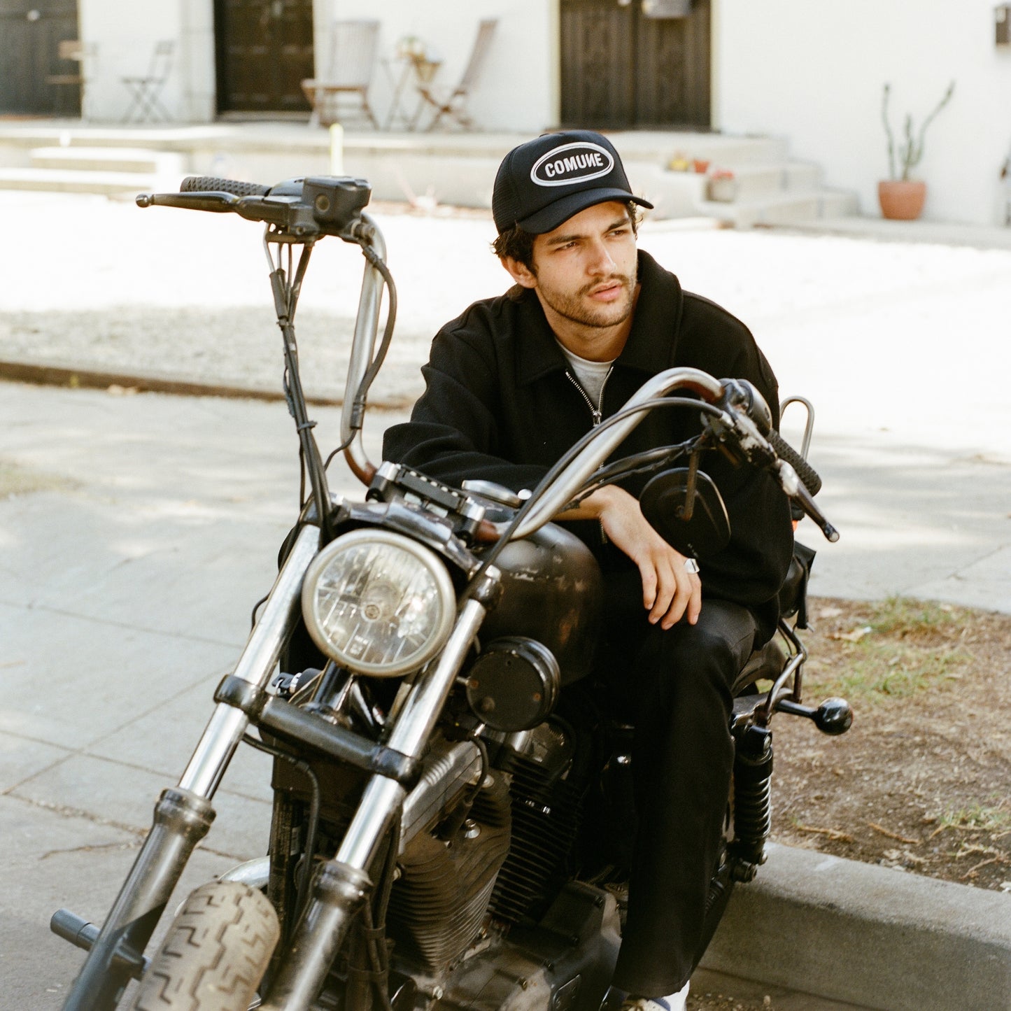 COMUNE artist Brandon sitting on a motorcycle wearing a cap with 'COMUNE' branding.