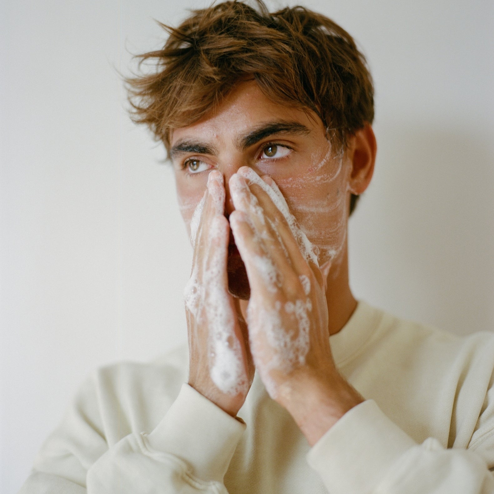 Man applying COMUNE Essentials Face Cleanser on his face with a neutral background