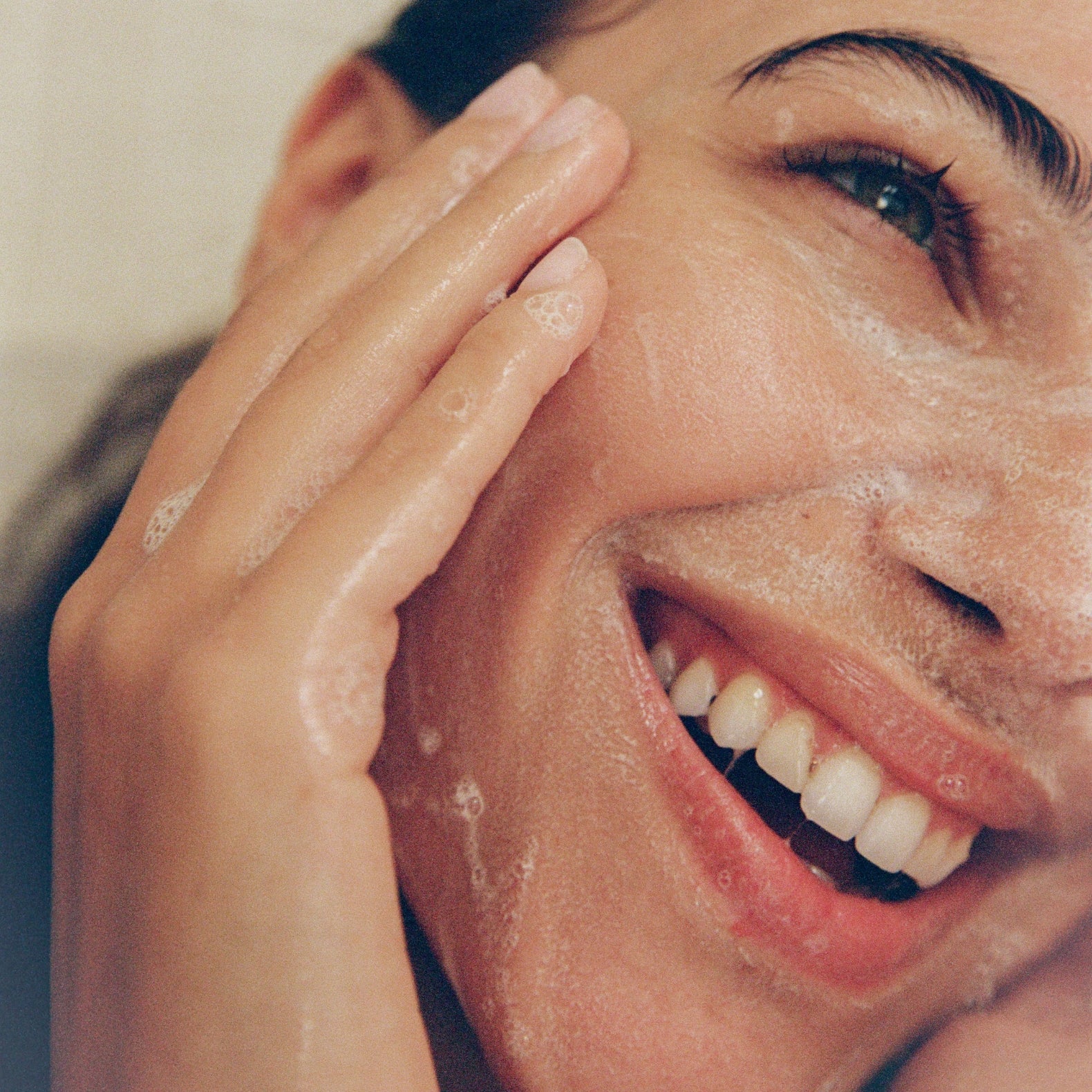 Women washing her face with a smile enjoying 'COMUNE' Essentials Face Cleanser