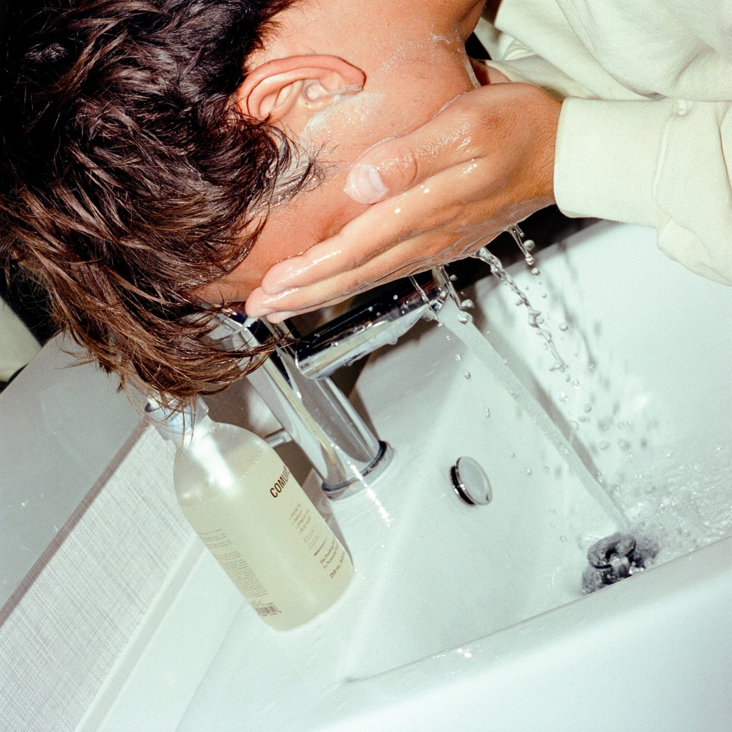 Men washing face after applying the gentle cleanser from COMUNE Essentials Face Cleanser over the sink for the ultimate cleansing.