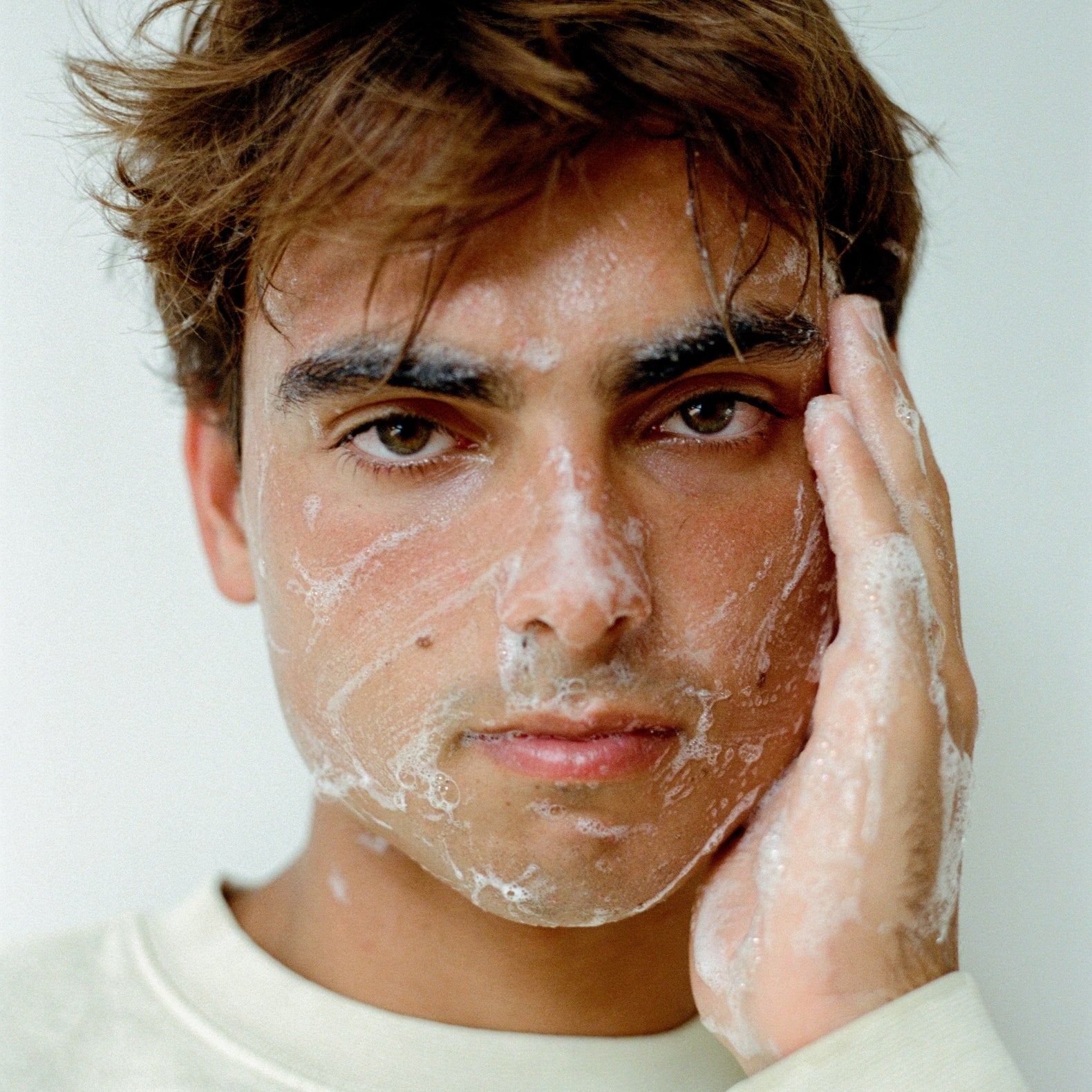 After days of surfing, man is applying COMUNE Essentials Face Cleanser on his face to cleanse surface impurities while revitalizing to help reveal clearer, healthier-looking skin.