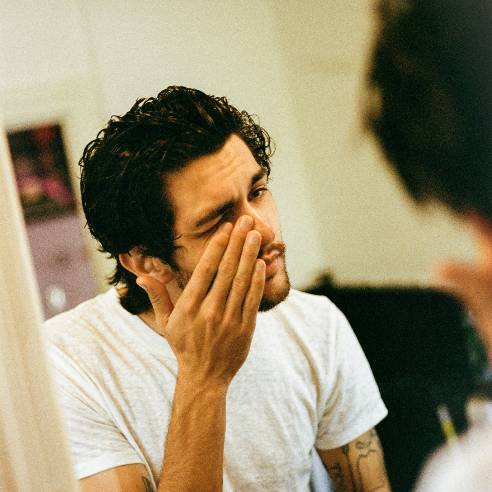 COMUNE artist looking at himself in a mirror, wearing a white t-shirt after applying 'COMUNE' Vita Boost Serum